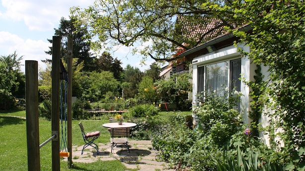 Un jardin avec une balançoire en bois, un banc et une table avec des chaises.