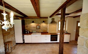 A kitchen with stone walls, wooden beams, a central island, and a hanging light fixture. - Exclusive 4-star holiday home for 8-12 people on historic Dreiseithof (Pirna)