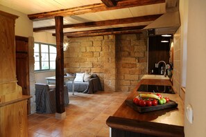 A rustic kitchen with stone walls, wooden beams, and a wooden counter with fresh produce. - Exclusive 4-star holiday home for 8-12 people on historic Dreiseithof (Pirna)