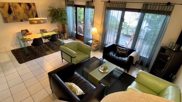 A modern living room with a glass coffee table, a sofa, a dining area with a table and chairs, and a large window with curtains.