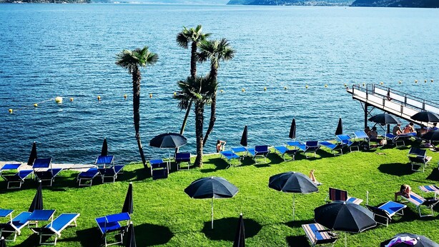 Un resort a orillas del lago con sillones de sol, sombrillas y una zona de piscina.