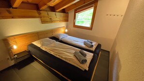 A room with two beds, wooden beams, a window, and a light fixture.
