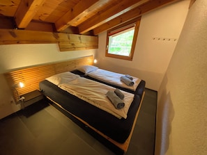Ein Zimmer mit zwei Betten, Holzbalken, einem Fenster und einer Lampe.