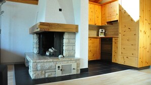 A stone fireplace with a wooden mantel, a kitchen with wooden cabinets, and a black tiled floor.