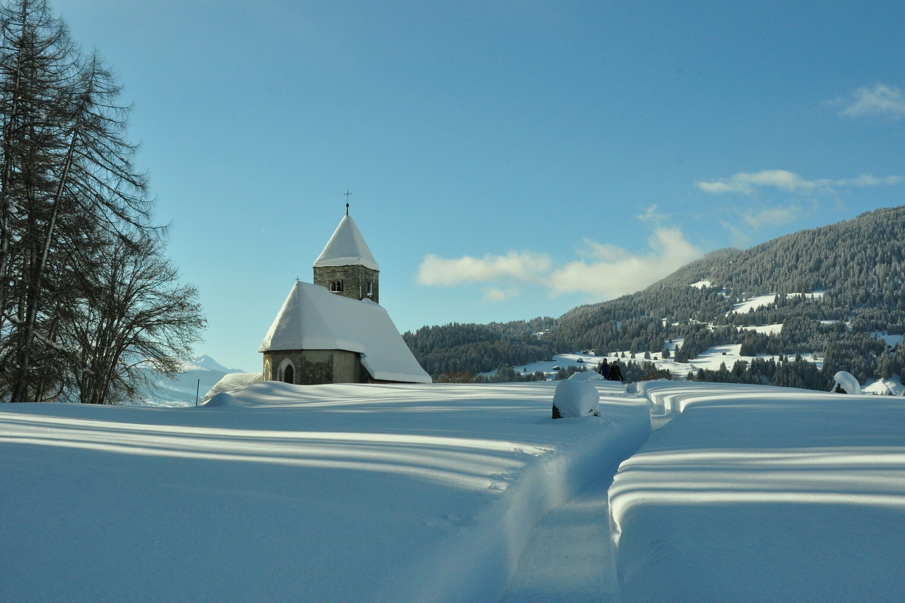 A snow-covered landscape with a church and a mountain in the background.