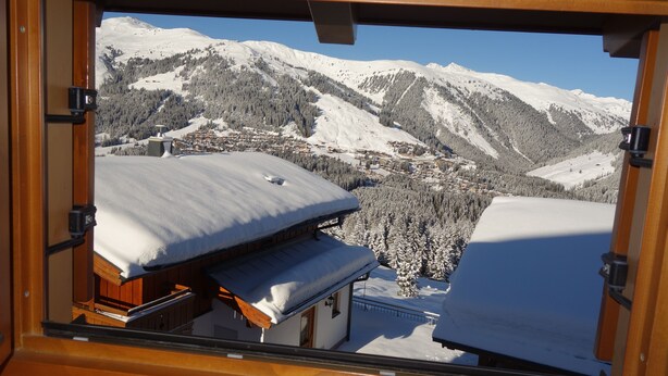 A window view of a mountain village with snow-covered roofs and buildings, surrounded by forested slopes and snow-covered mountains. - Luxury 10 people hpuse near to a lift and loipe, 1700 m high (Krimml)