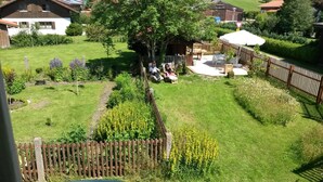 En lukket have med træhegn, blomsterbede med gule blomster og en terrasse med havemøbler.