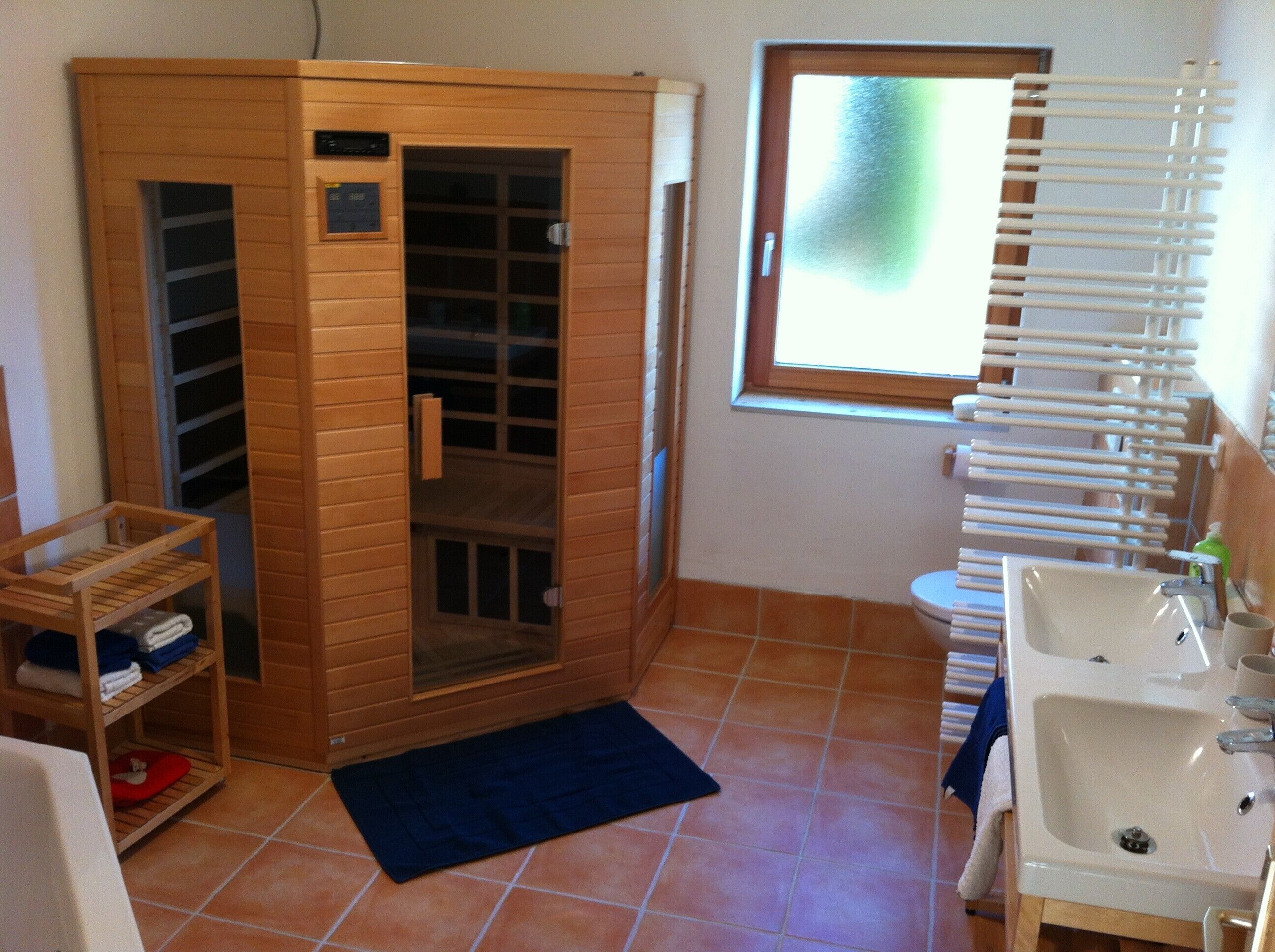 A bathroom with a wooden sauna, a window with blinds, and a sink with a mirror.