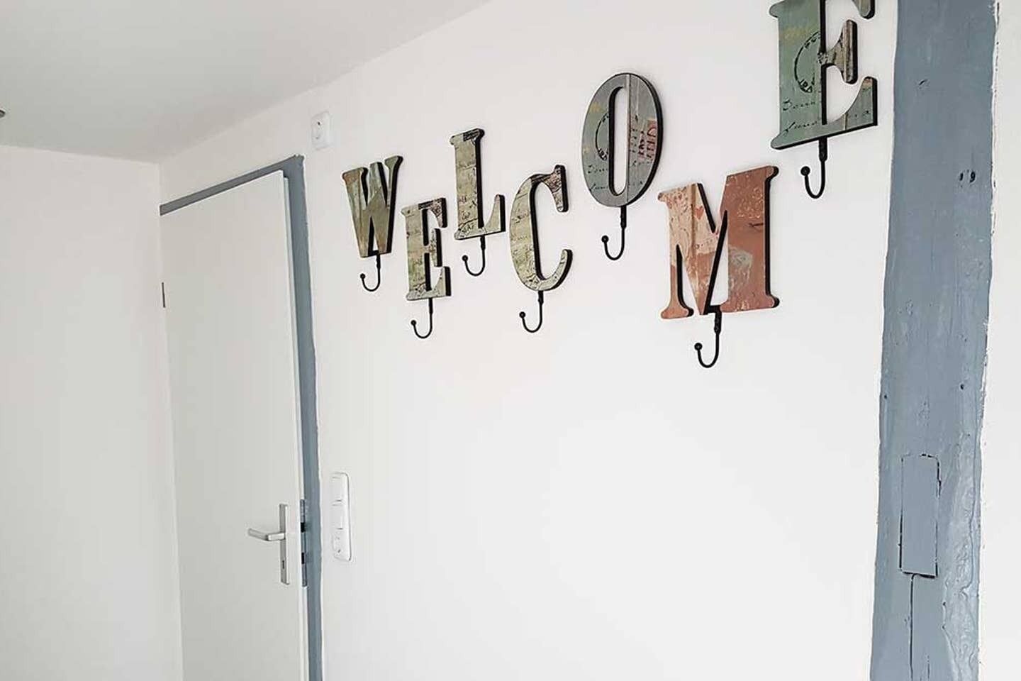 Eine Wand, auf der das Wort „WILLKOMMEN“ aus Metallbuchstaben mit Haken angebracht ist.