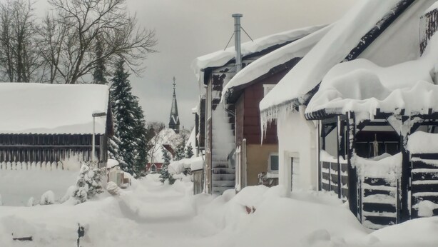 Zona residencial nevada con casas, una iglesia y una chimenea alta.