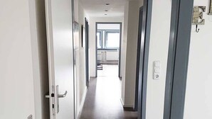 Un pasillo con paredes blancas, suelo de madera y una ventana al final.