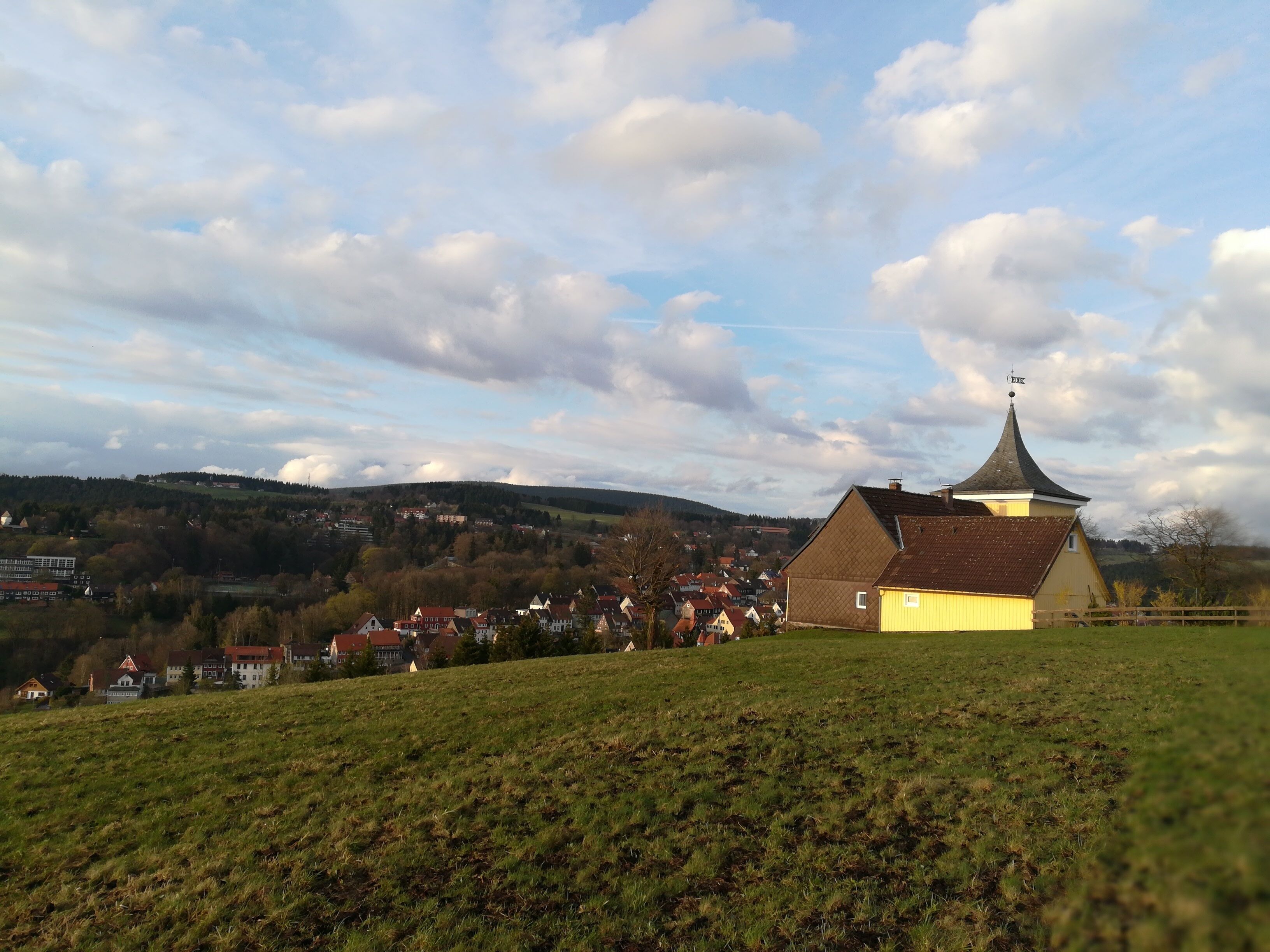 Una iglesia con un campanario puntiagudo sobre una colina que domina un pueblo.