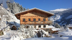 Eine Holzhütte mit Balkon, umgeben von schneebedeckten Bäumen und Bergen.