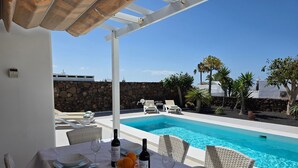 A poolside dining area with a table set for two, two bottles of wine, and a bowl of oranges. - Beautiful house with solarheated and private pool (Tias)