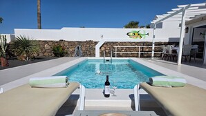 A pool area with lounge chairs, a bottle of wine, and a decorative bowl on a table. - Beautiful house with solarheated and private pool (Tias)