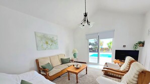A living room with a sofa, armchair, coffee table, TV, and a sliding glass door leading to a pool. - Beautiful house with solarheated and private pool (Tias)