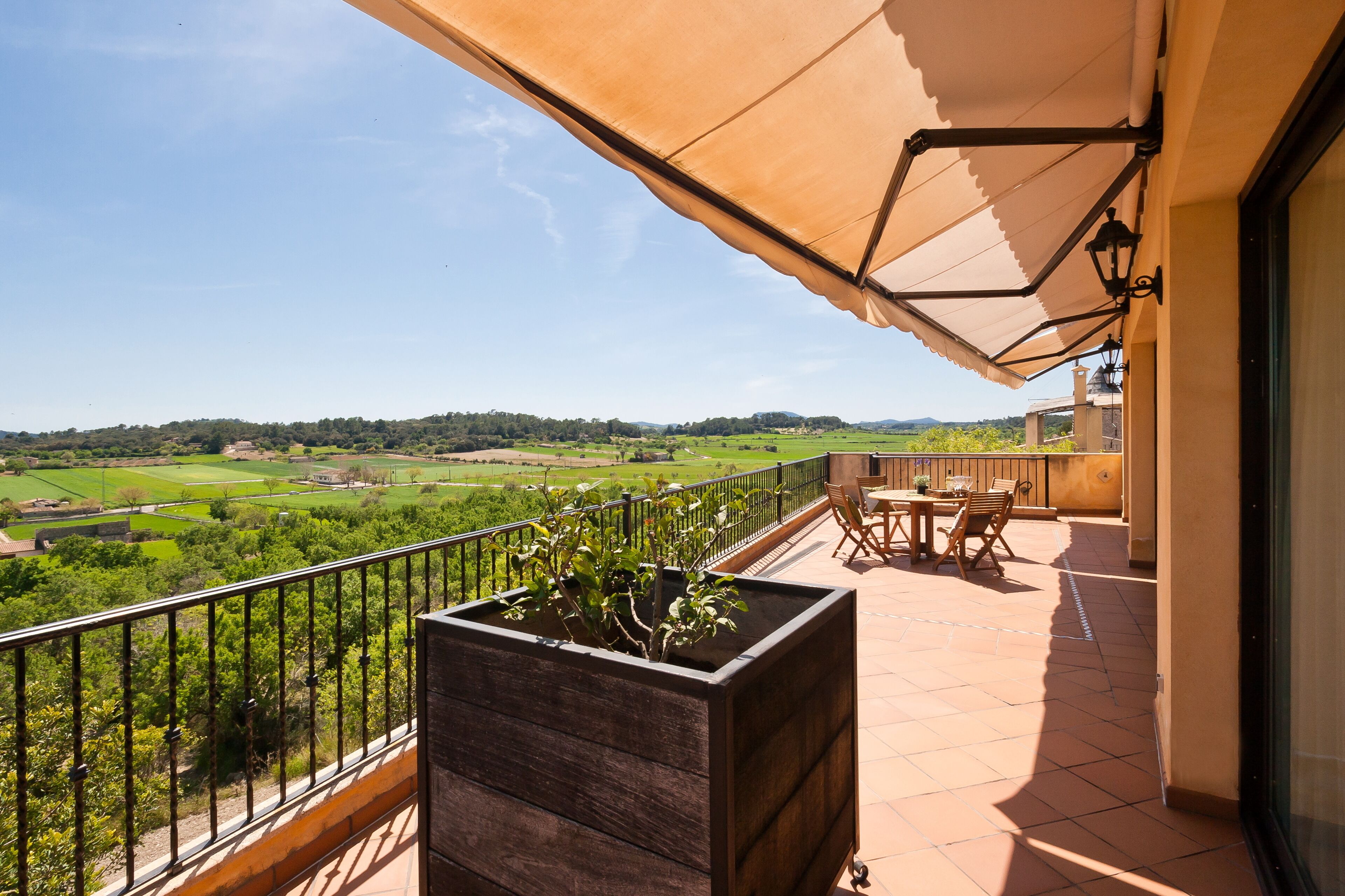 Un balcon donnant sur un paysage verdoyant, agrémenté d’un jardinier en bois et de mobilier d’extérieur.