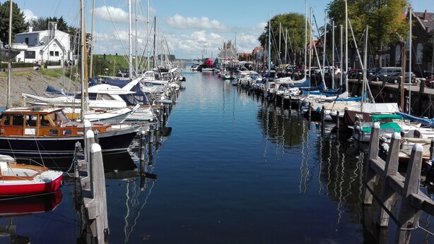 A marina with boats docked along a calm waterway, surrounded by buildings and trees. - «Het Fitschhuisje» Cozy cottage in the park "De Kreek" - Free Wi-Fi (Bruinisse)
