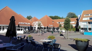 An outdoor seating area with tables and chairs, a 'CENTRUM' and 'PLAZA' sign, and a building with a red-tiled roof. - «Het Fitschhuisje» Cozy cottage in the park "De Kreek" - Free Wi-Fi (Bruinisse)
