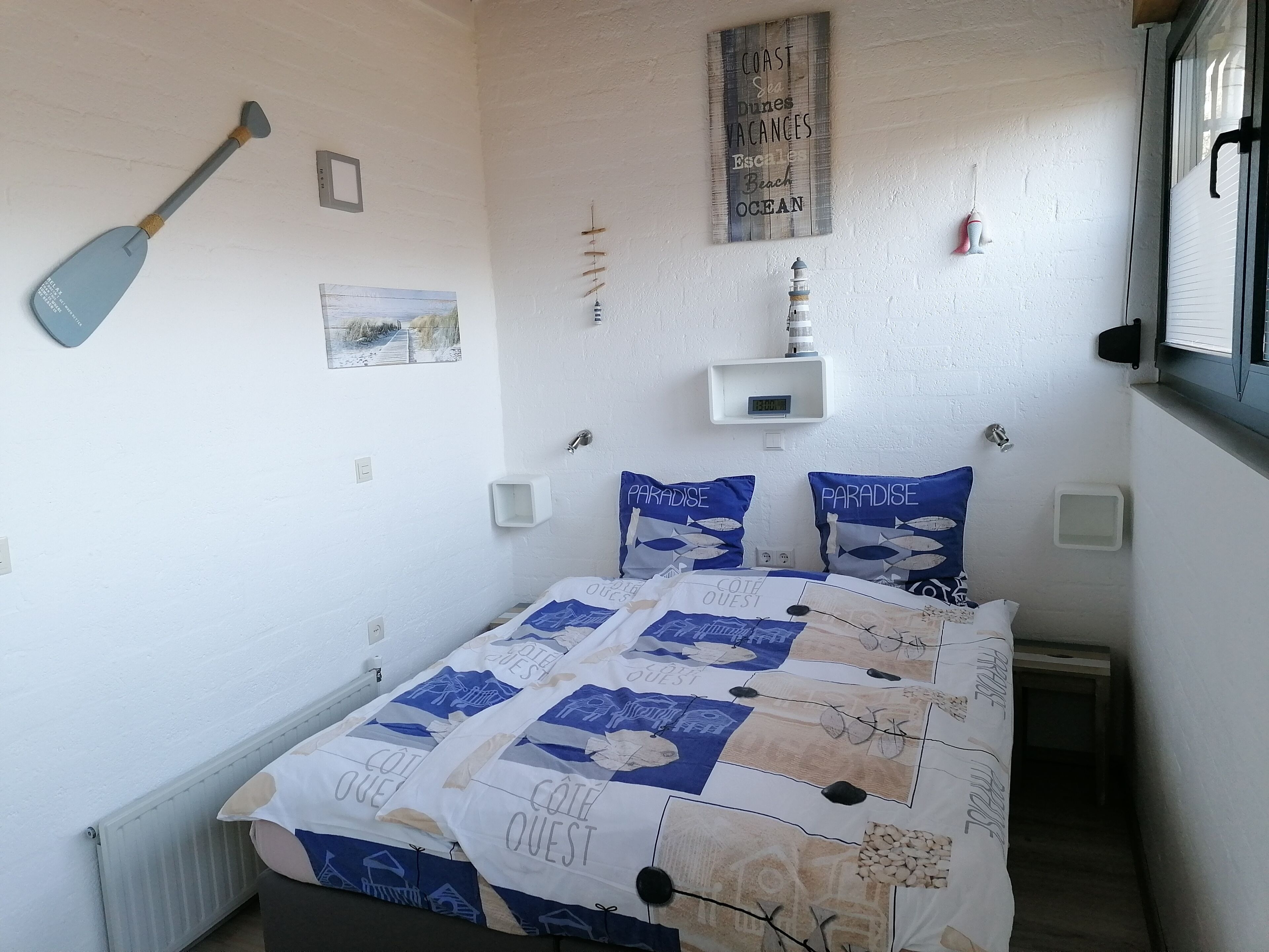 Ein Schlafzimmer mit einem Bett, einer Wanduhr, einem kleinen Regal und einem Schild mit der Aufschrift 'COAST Dunes Vacances'.