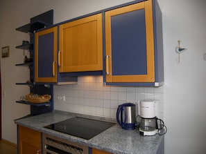 A kitchen with wooden cabinets, a built-in oven, a coffee maker, and a kettle on the countertop.