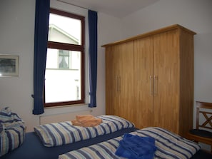 A bedroom with two beds, a wooden wardrobe, a window with curtains, and a radiator.