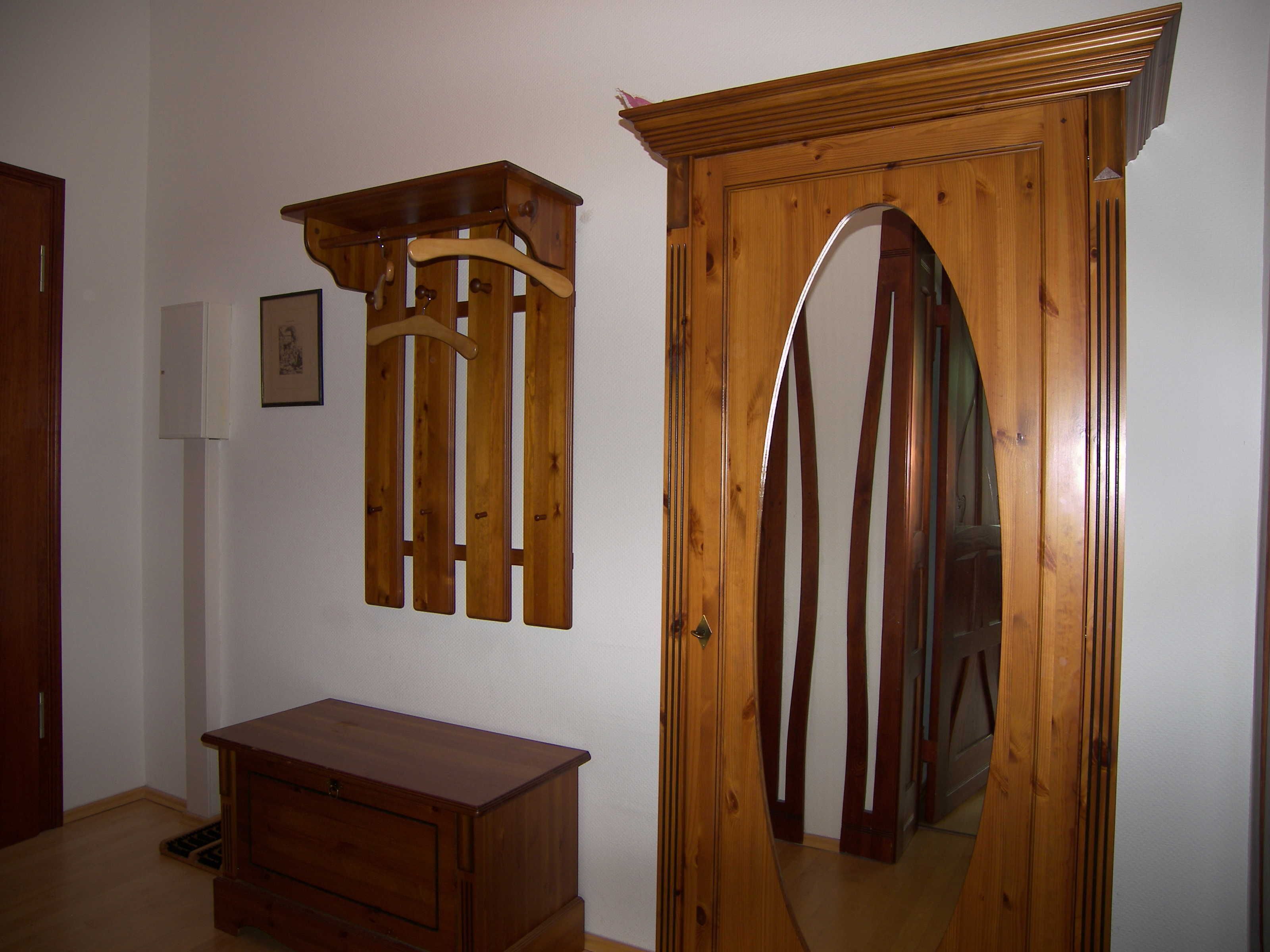 A room with a wooden door, a small wooden dresser, and a wall-mounted wooden shelf.
