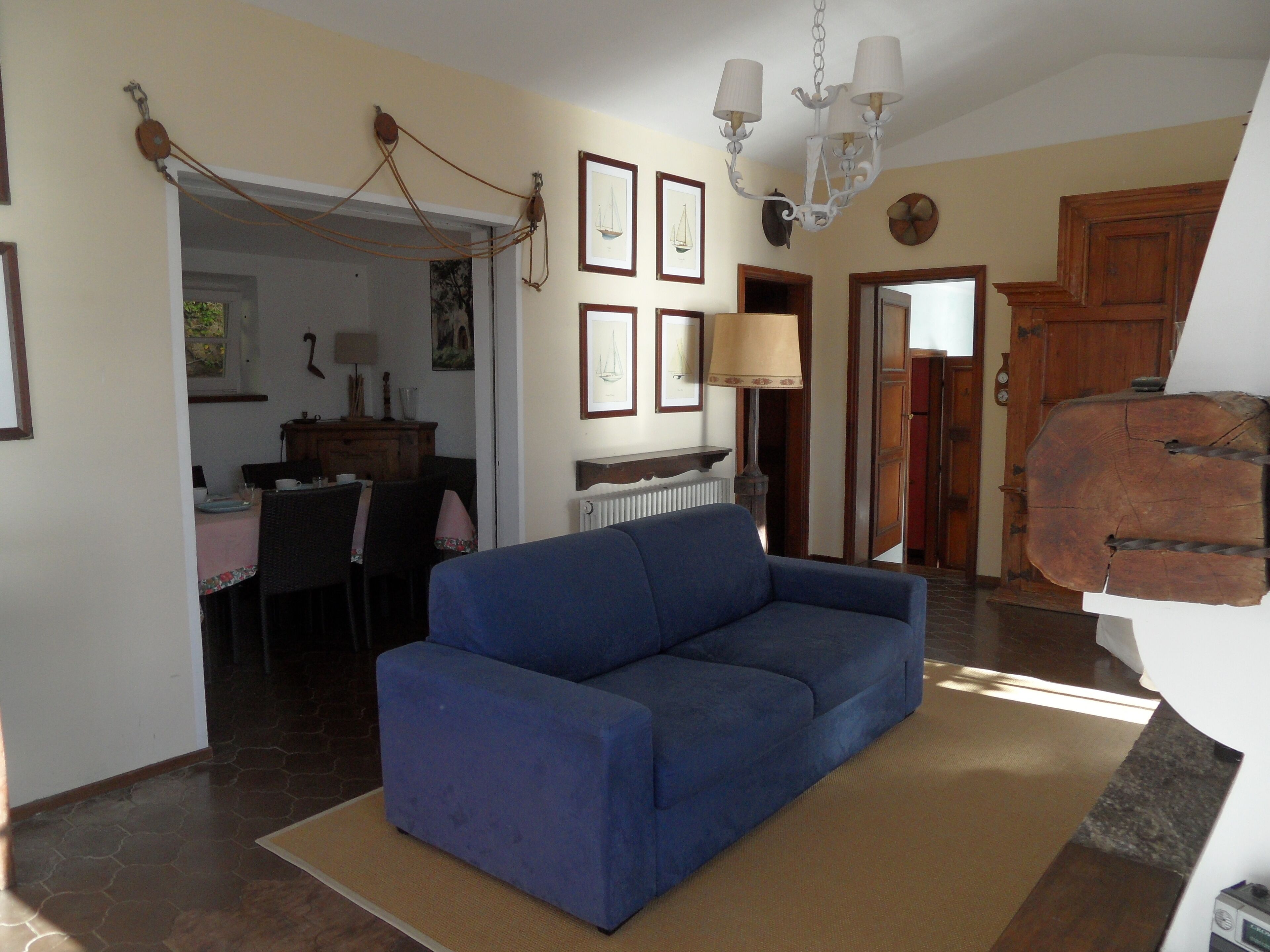 A living room with a blue sofa, a dining area with a table and chairs, and a kitchen visible through an open door.