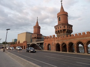 Ein historisches Gebäude aus rotem Backstein mit zwei markanten Türmen und einer Brücke, die zu einem modernen Gebäude führt.