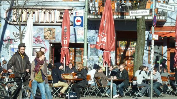 A street scene with outdoor seating, bicycles, and a building with graffiti and signage. - Central and quiet - a view of the countryside (Berlin)