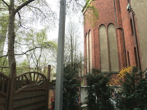 Ein Backsteinhaus mit Rundbogenfenstern, umgeben von Bäumen und einem hölzernen Tor.