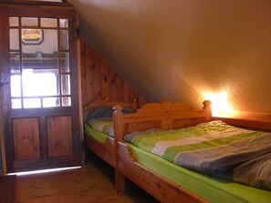 Une petite pièce agréable, dotée d’une porte en bois et d’un lit simple recouvert d’une couverture à rayures vertes et blanches.
