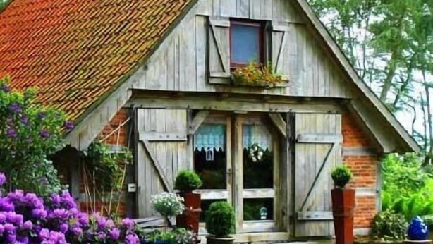 Una casa rústica de madera con techo inclinado, un porche delantero y plantas en macetas.