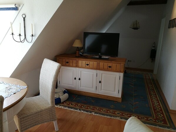 Una habitación acogedora con un televisor sobre un mueble de madera, una silla de mimbre y una alfombra estampada.