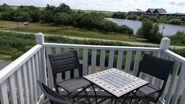 Una terrazza con tavolo e quattro sedie, vista su un corpo d'acqua e vegetazione.