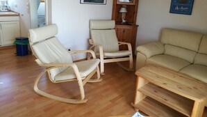 Un soggiorno con un divano, due poltrone a dondolo, un tavolino in legno e un mobile contenitore con una lampada.