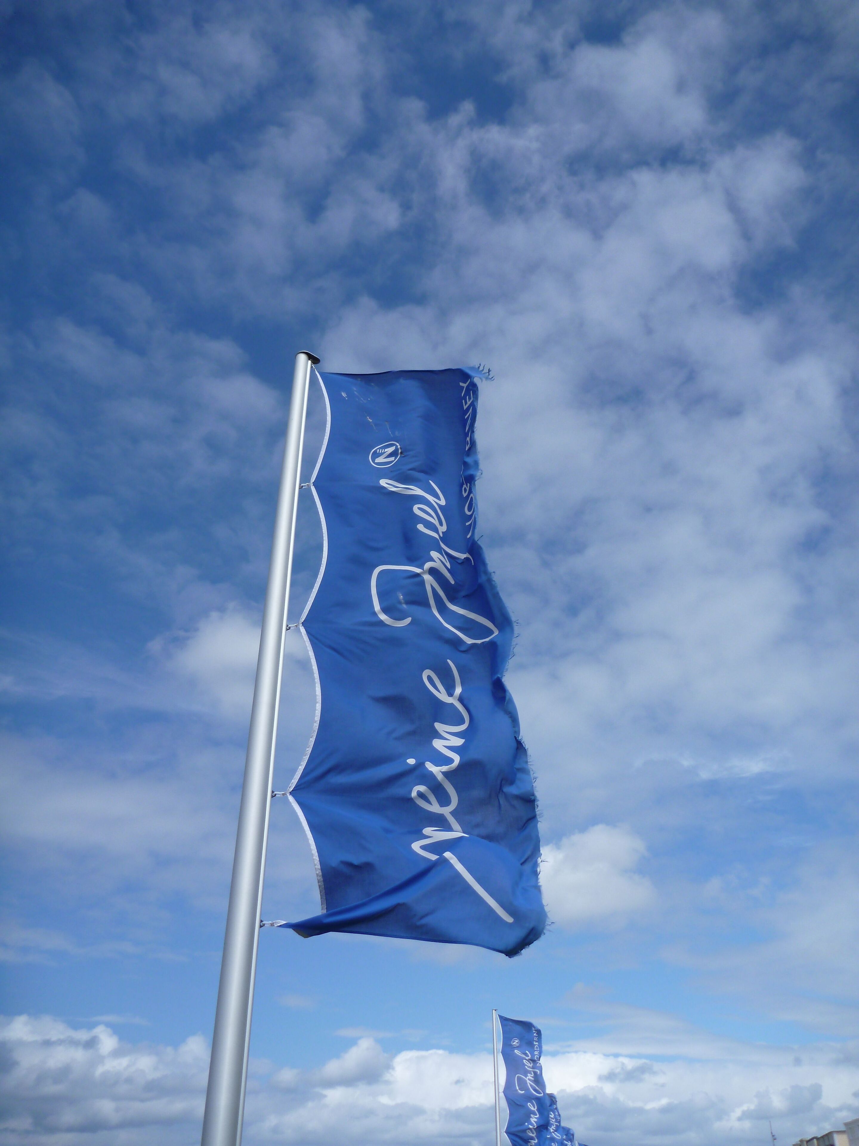 A flag with the text "Kleine Freude" on a flagpole against a partly cloudy sky.