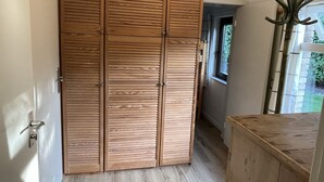 Ein Holzkleiderkasten mit horizontalen Lamellen, eine Holzbank und ein Fenster mit Blick ins Grüne.