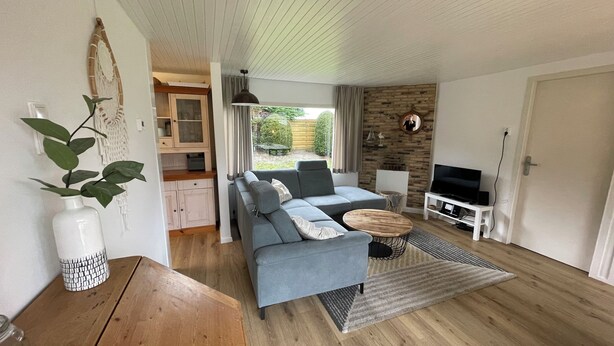 Ein modernes Wohnzimmer mit einem grauen Sofa, einem Holztisch und einem Fernseher auf einem weißen Schrank.