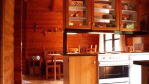 A wooden cabin interior with a kitchen area featuring a stove, cabinets, and a dining table with chairs.
