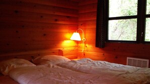 A wooden cabin room with a bed, a nightstand, and a window with a view of trees.