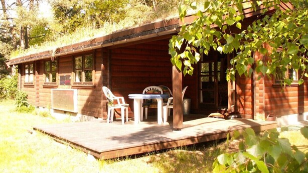 A wooden cabin with a porch, a table, and chairs.