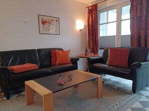 A living room with two black leather sofas, a wooden coffee table, a small round table with a bottle and glass, and a framed artwork on the wall.