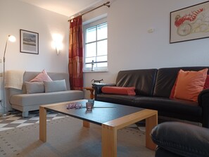 A living room with a sofa, a black leather couch, a wooden coffee table, and a patterned rug.