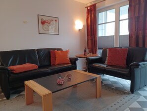 Ein Wohnzimmer mit zwei schwarzen Ledersofas, einem Holztisch, einem kleinen runden Tisch mit Flasche und Glas sowie einem gerahmten Kunstwerk an der Wand.
