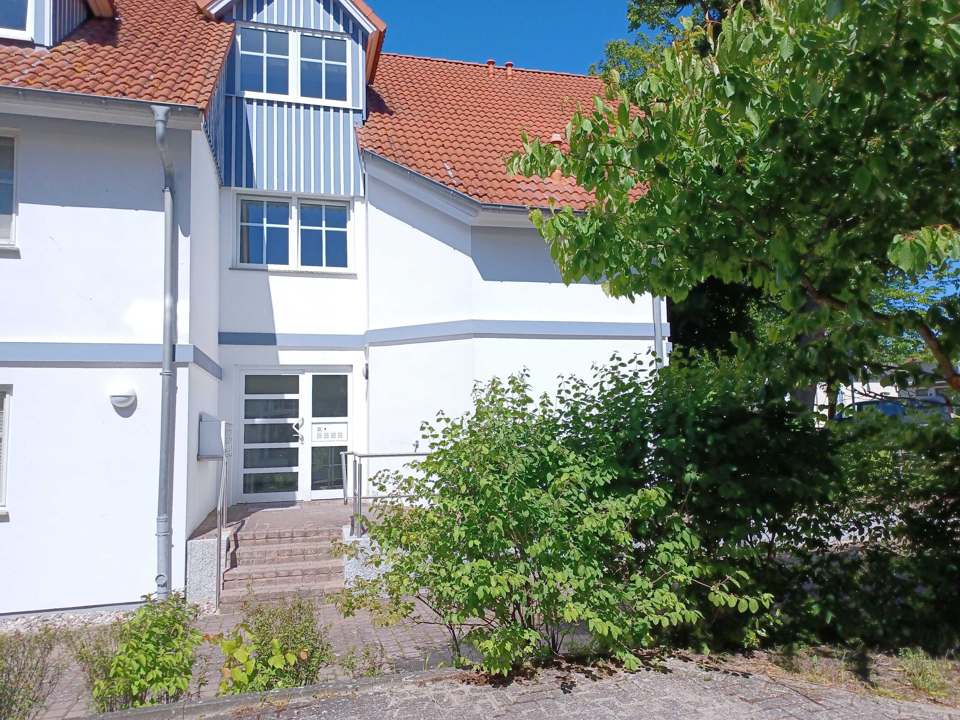 A two-story building with a red-tiled roof, a white facade, and a staircase leading to the entrance.