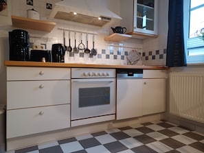 Eine Küche mit Schachbrettfußboden, weißen Schränken, einem Siemens Geschirrspüler, einem Herd und einer Kaffeemaschine.