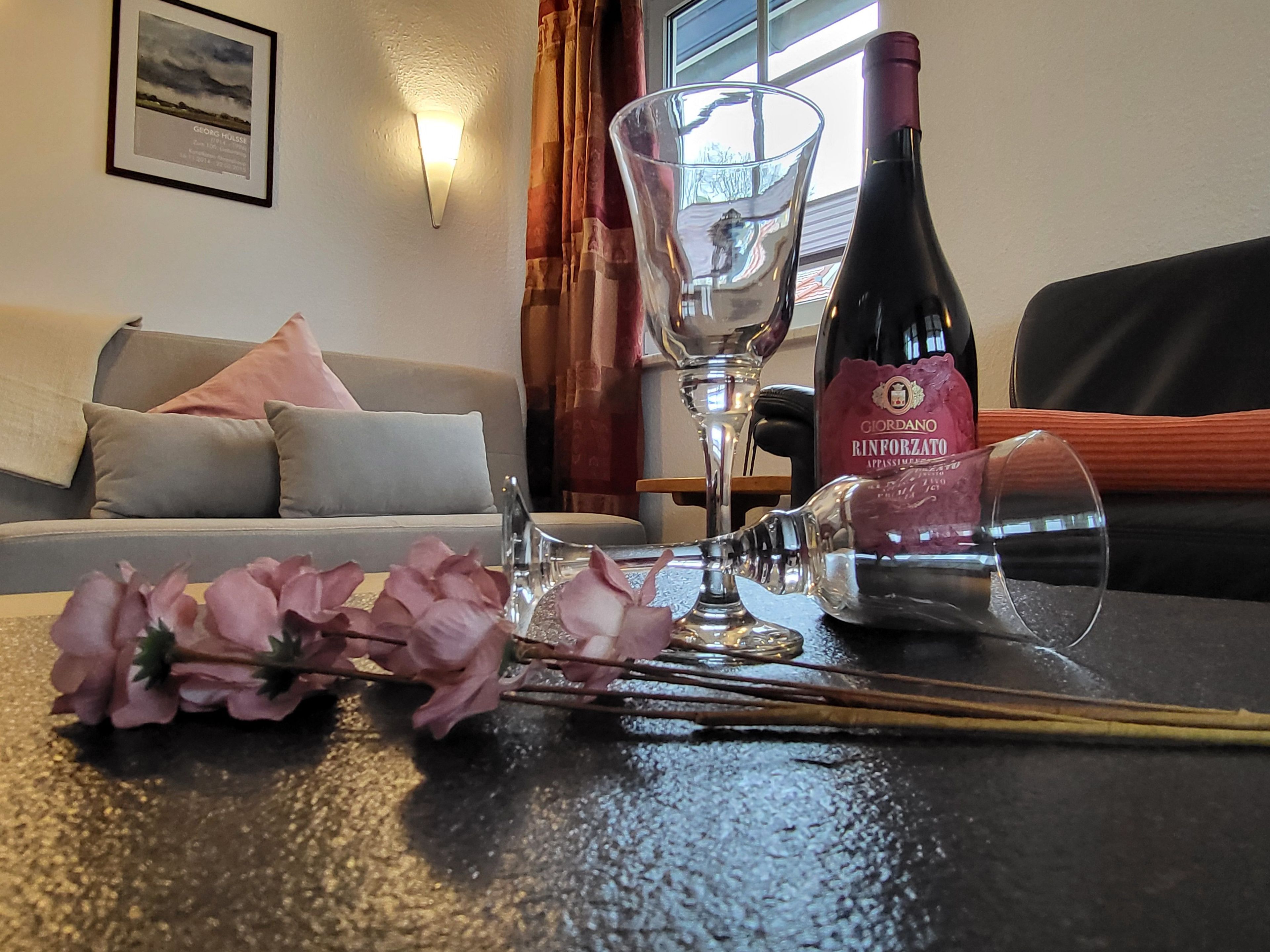 A room with a sofa, a table with a wine bottle, glasses, and flowers.