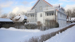 Una casa de dos pisos con un balcón, un techo cubierto de nieve y un cielo despejado.
