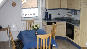 A small kitchen with a dining table, chairs, a vase with flowers, and a window with curtains. - cozy 3-room apartment in Timmendorf-Strand with sea view (Timmendorf-Strand)
